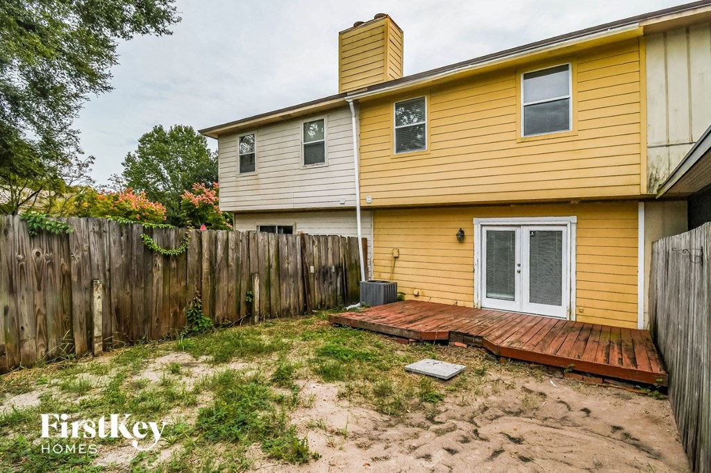 a backyard with a wooden deck and a yellow house