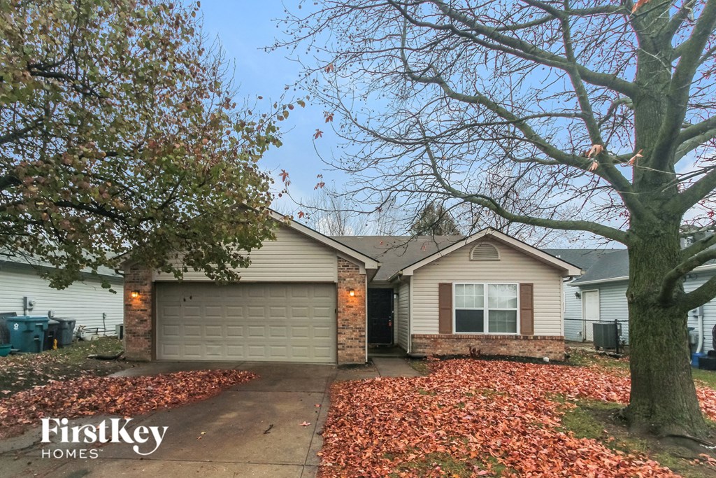 A house with a garage and a tree with orange leaves in front of it.