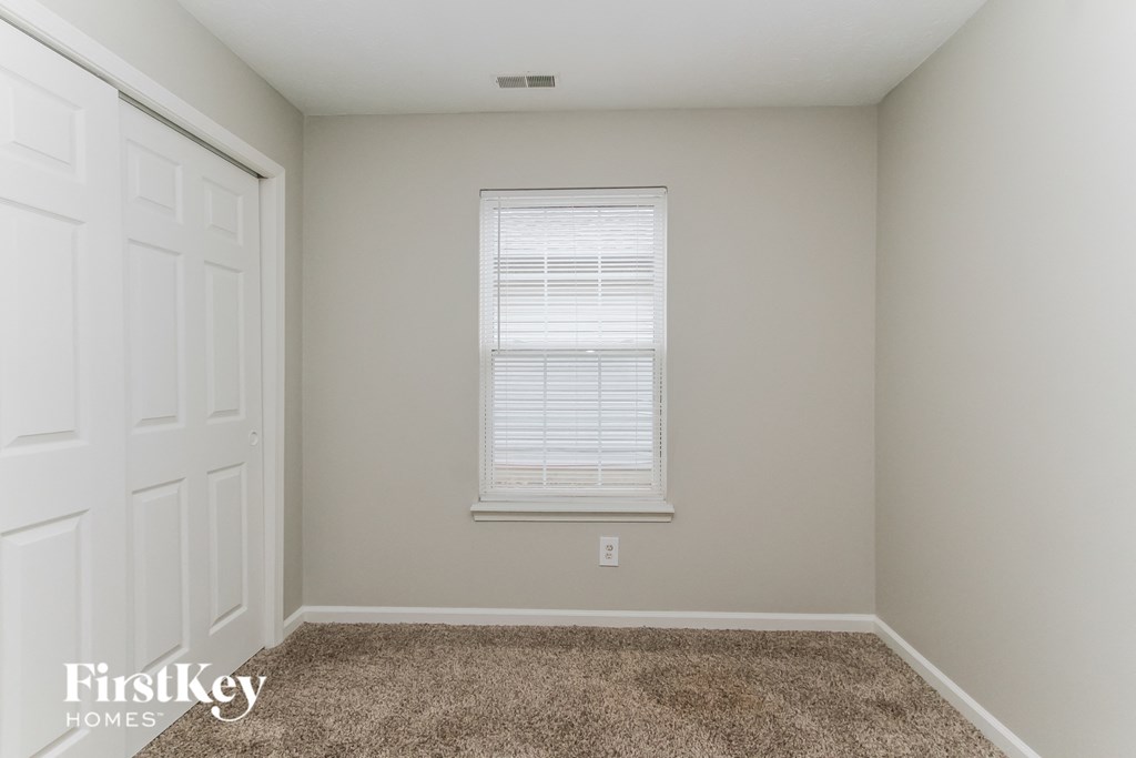A room with a carpeted floor, a window with blinds, and a white door.