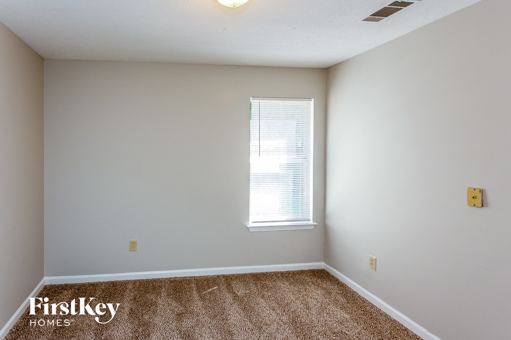 a bedroom with white walls and carpet and a window