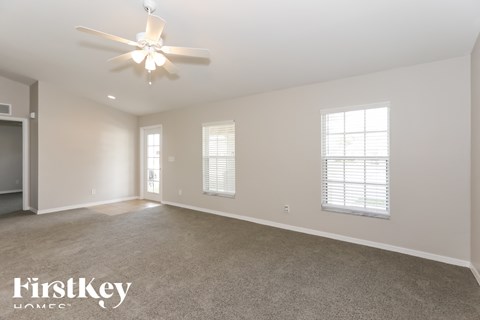 A spacious room with a ceiling fan and two windows.