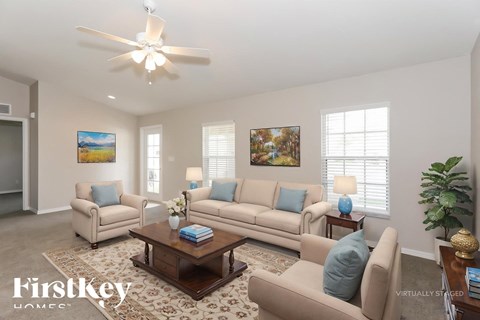 A living room with a beige sofa, two armchairs, a coffee table, and a ceiling fan.