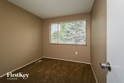 A room with a carpeted floor and a window showing trees outside.