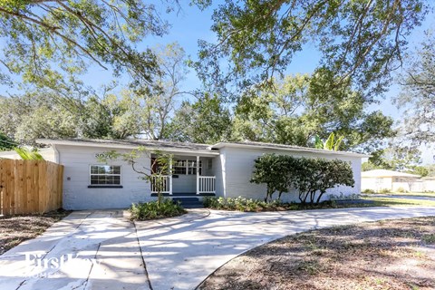 a small white house with a driveway and trees