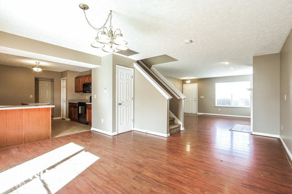 A large open living room with wood floors and a staircase leading to another room.