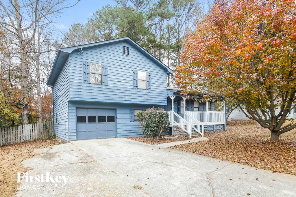 A blue house with a garage and a tree with orange leaves.