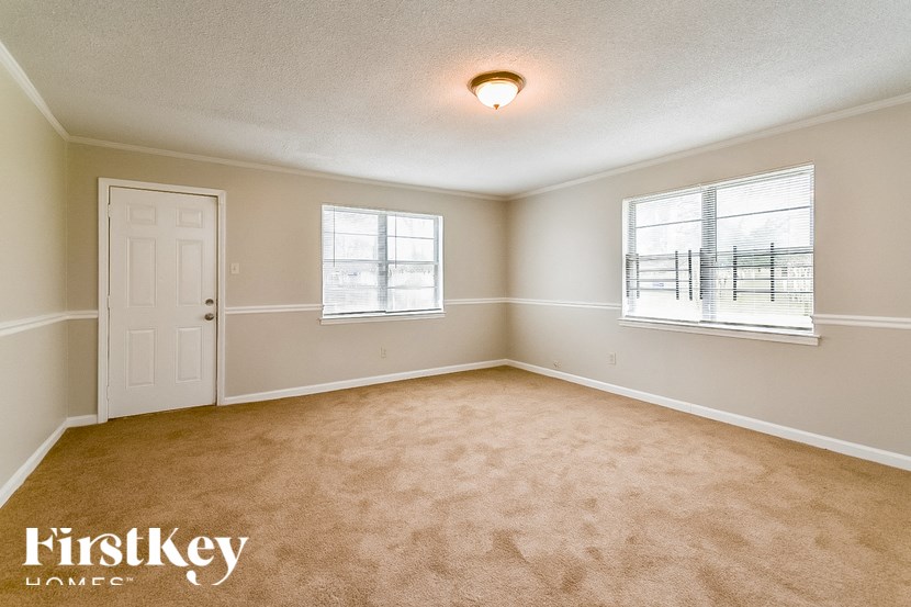 A room with a carpeted floor and two windows.