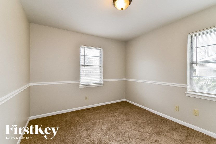 A room with a carpeted floor, a window with blinds, and a light fixture on the ceiling.