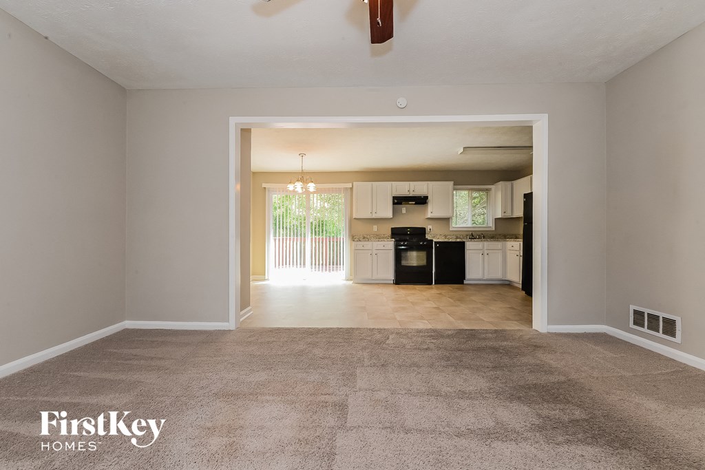 an empty living room with a kitchen in the background