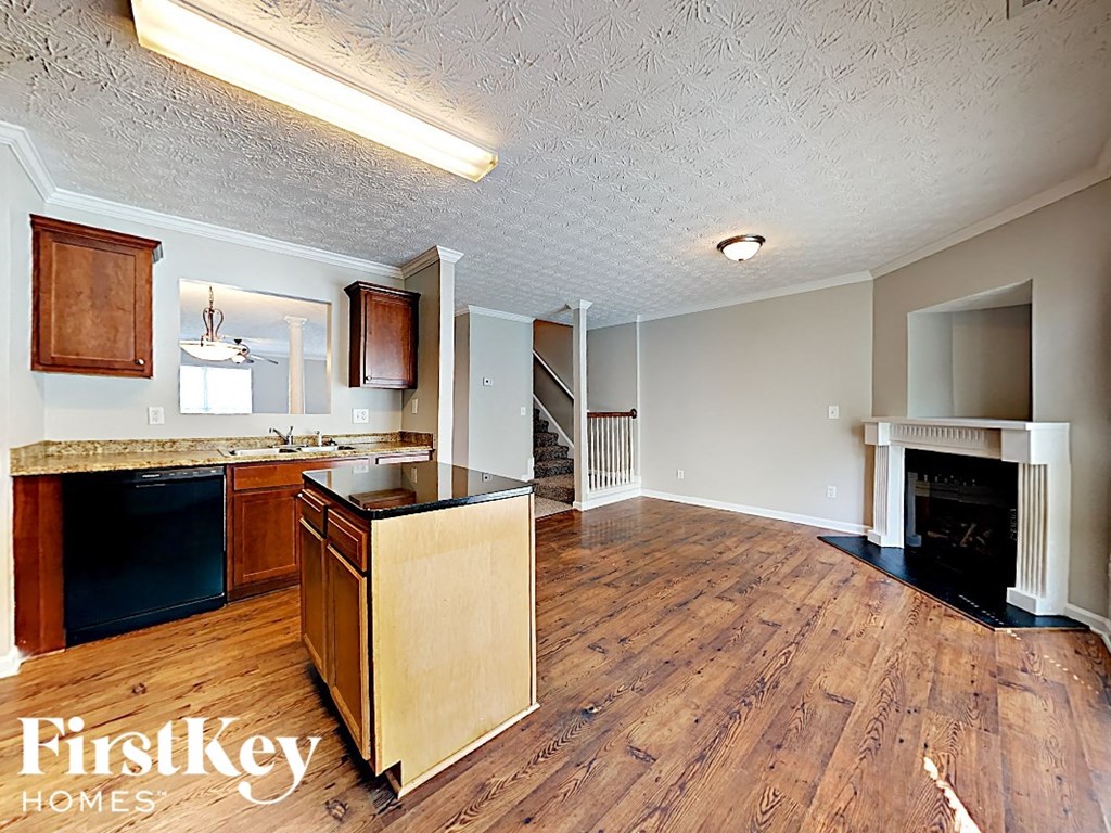 A kitchen with wooden floors and a fireplace in the living room.