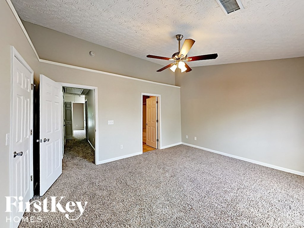 A carpeted room with a ceiling fan and a doorway leading to another room.
