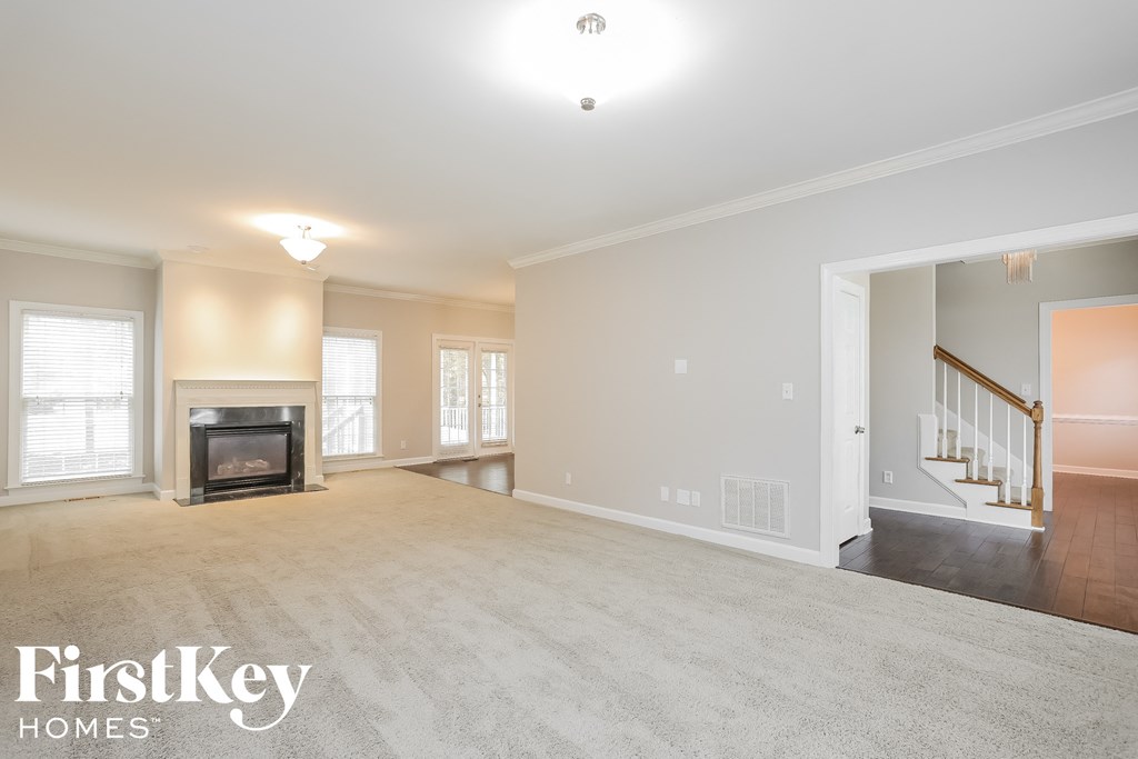 A spacious living room with a fireplace and a staircase in the background.