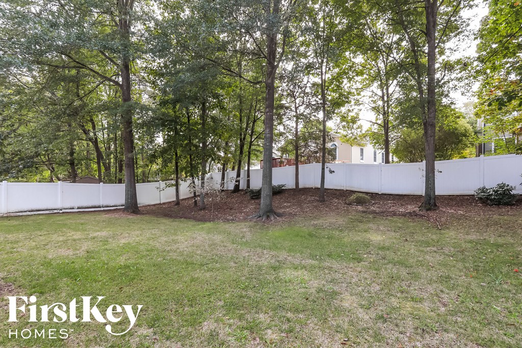 A white fence encloses a grassy yard with trees.