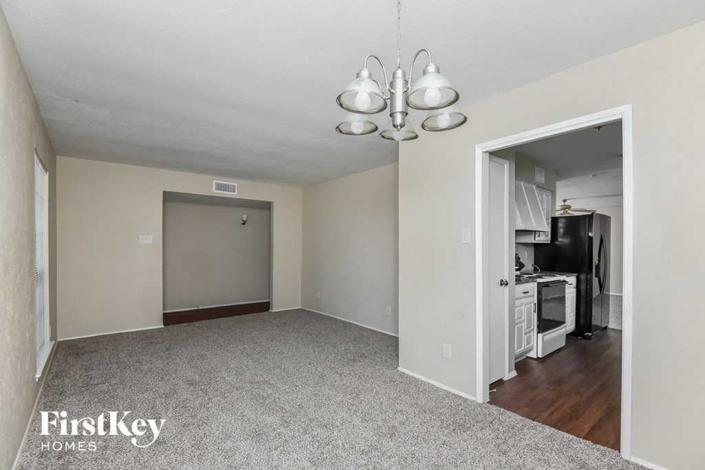 an empty living room with a door to the kitchen and a chandelier