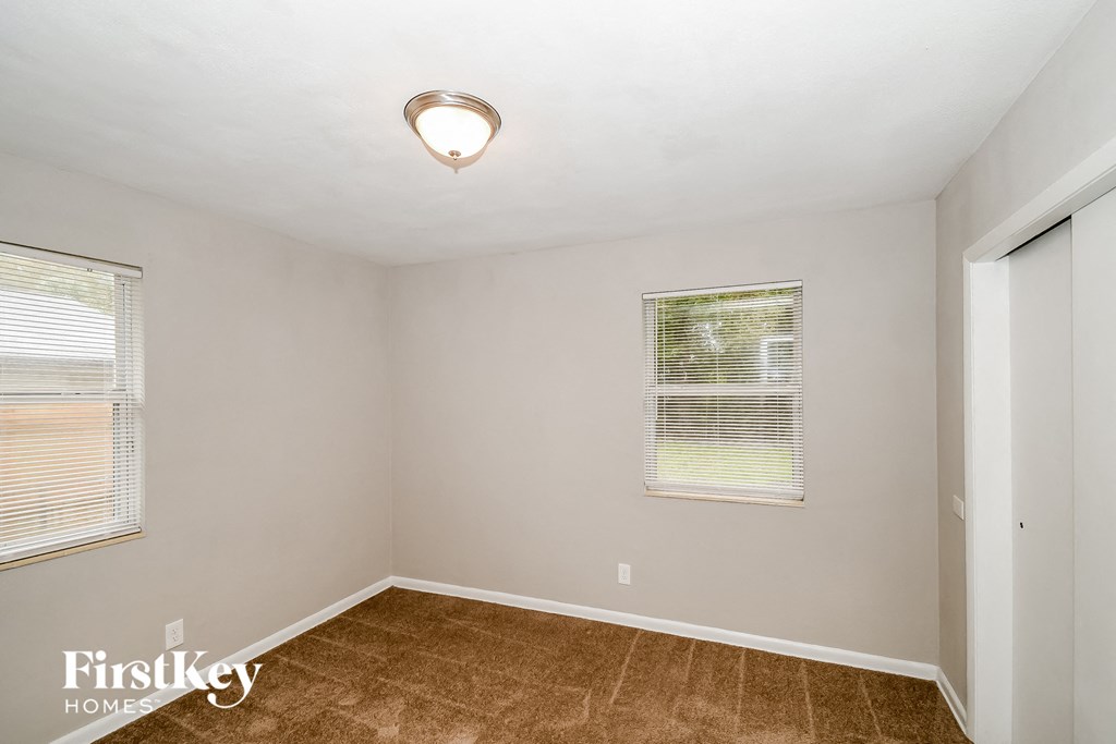 a bedroom with a large window and a brown carpeted floor