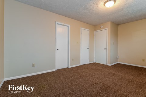 the living room of an apartment with carpet and two doors