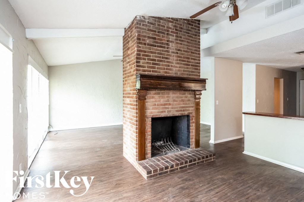 A brick fireplace in a room with wooden floors and white walls.