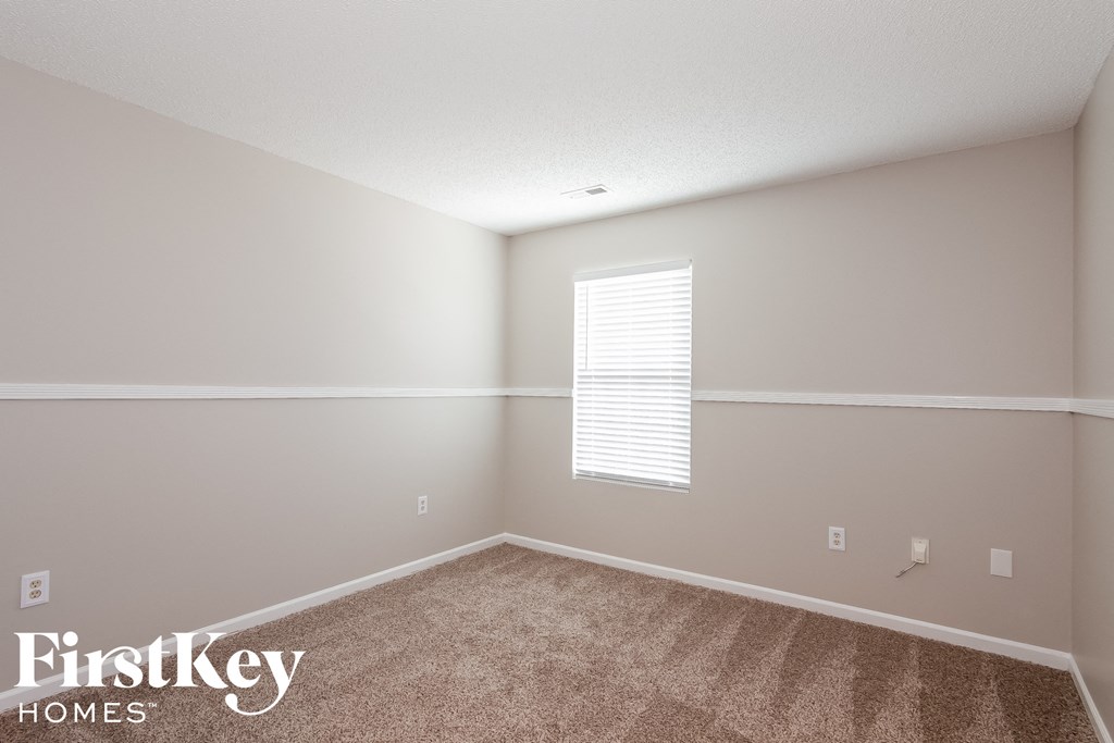 a bedroom with carpet and white walls and a window