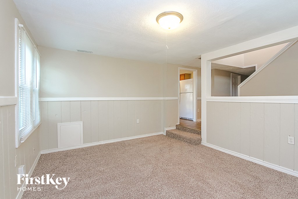 A spacious room with a carpeted floor and a staircase leading to another room.