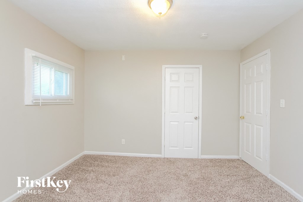 A room with a carpeted floor, two doors, and a window with blinds.