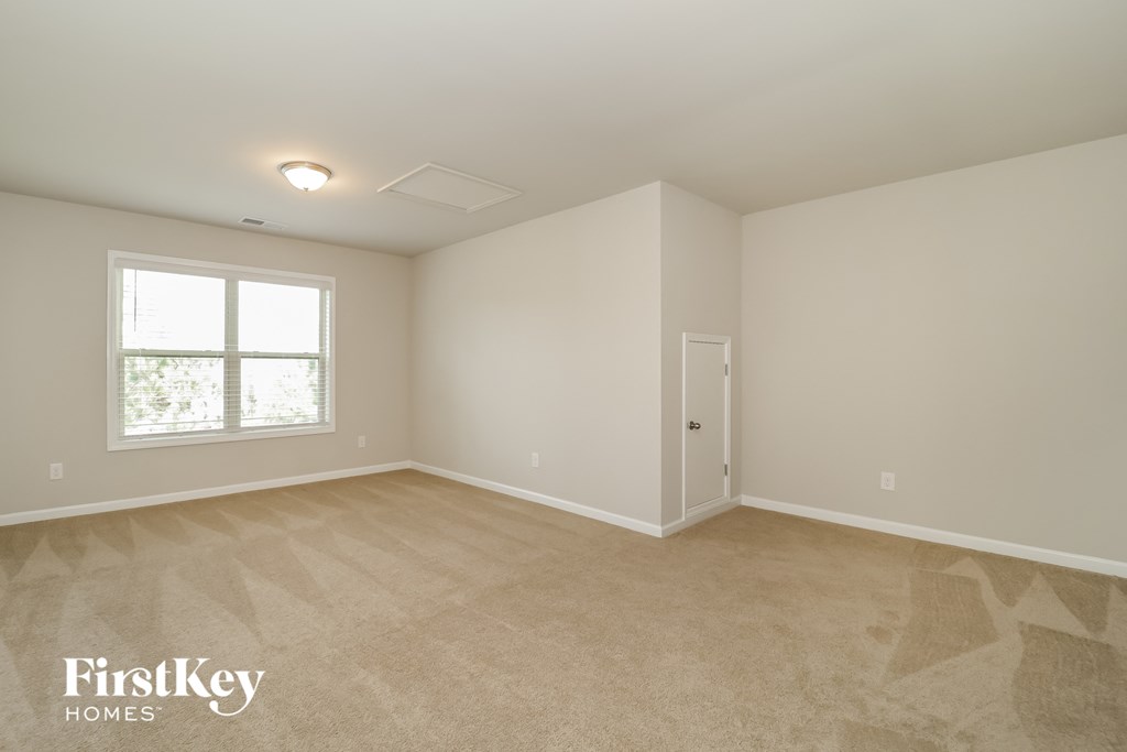 a bedroom with white walls and beige carpet and a window