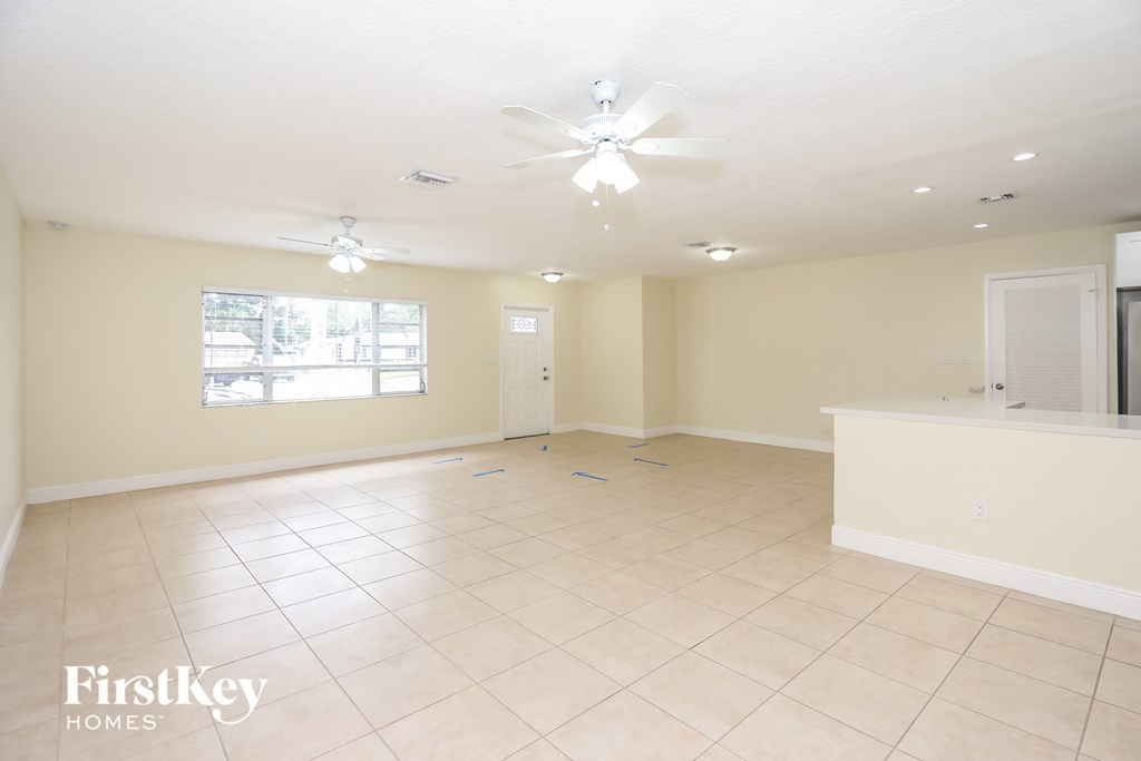 an empty living room with a kitchen and a ceiling fan