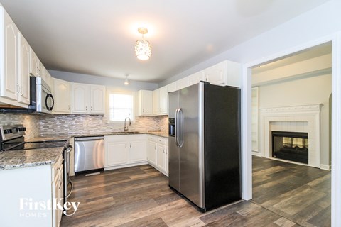A kitchen with a black fridge and a fireplace in the background.
