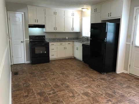 A kitchen with black appliances and brown tiled flooring.