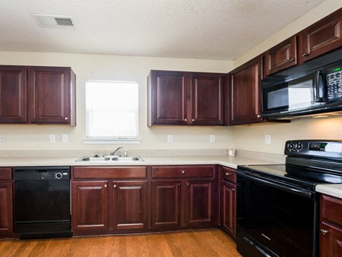 A kitchen with dark wood cabinets and black appliances.