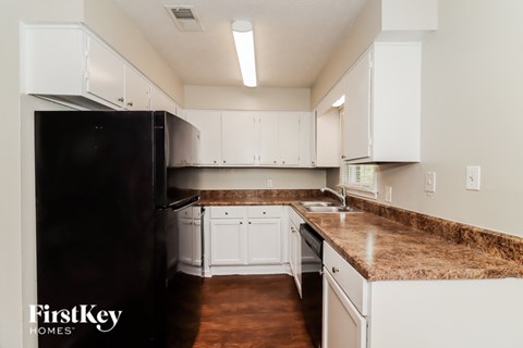 A black refrigerator is in a kitchen with white cabinets.