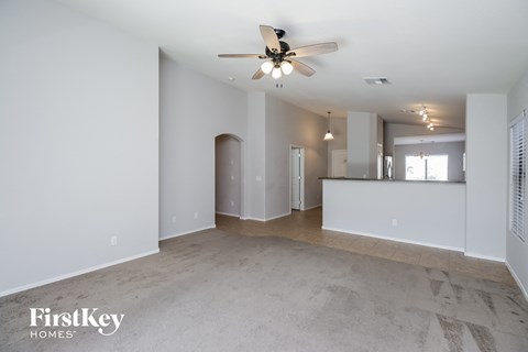 an empty living room with a ceiling fan and a kitchen