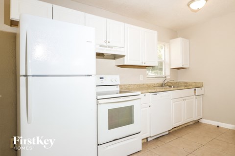 A white refrigerator is in a kitchen with white cabinets.