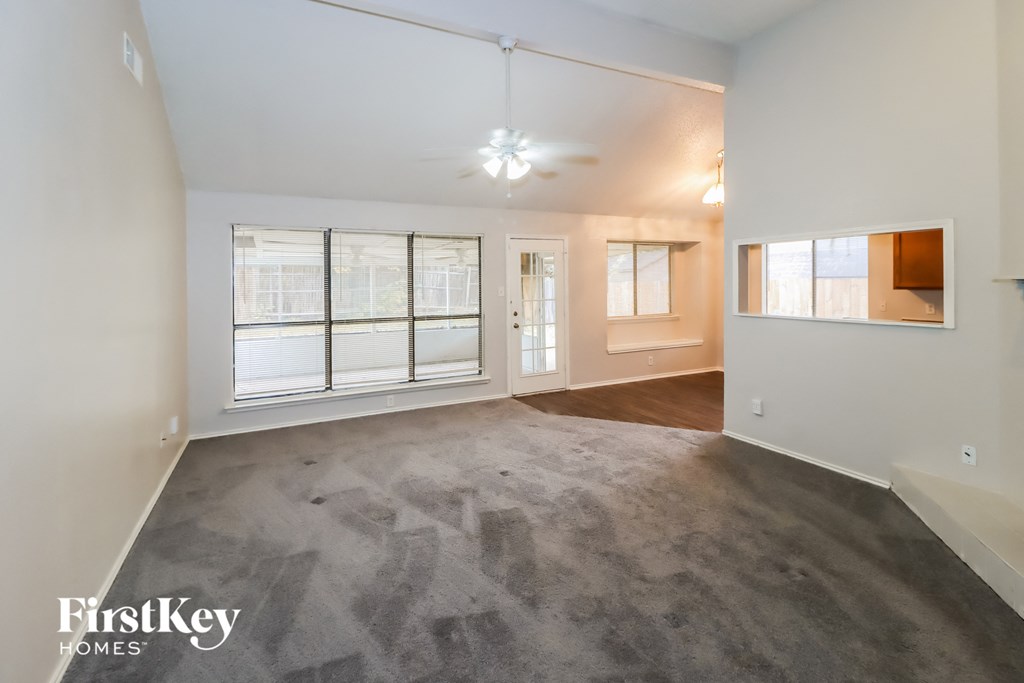 an empty living room with a large window and a ceiling fan