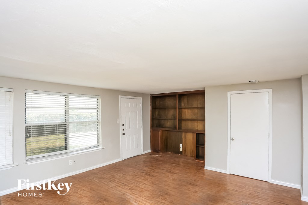 an empty living room with a large window and a wooden book shelf