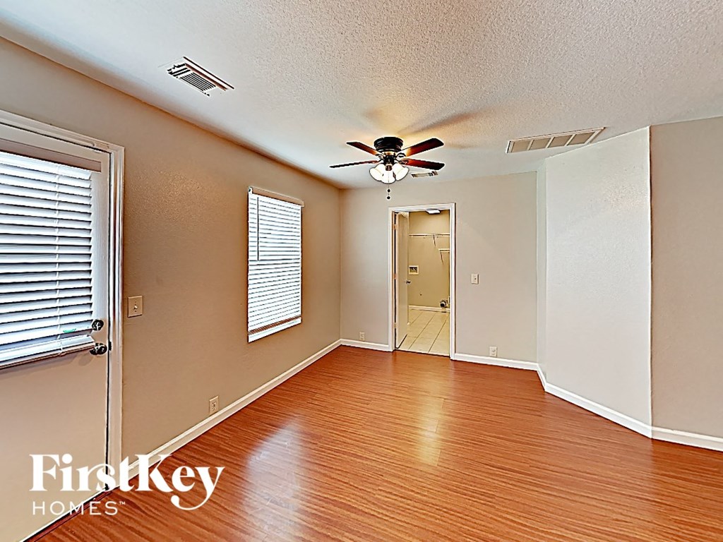 an empty living room with a ceiling fan and a door to a hallway
