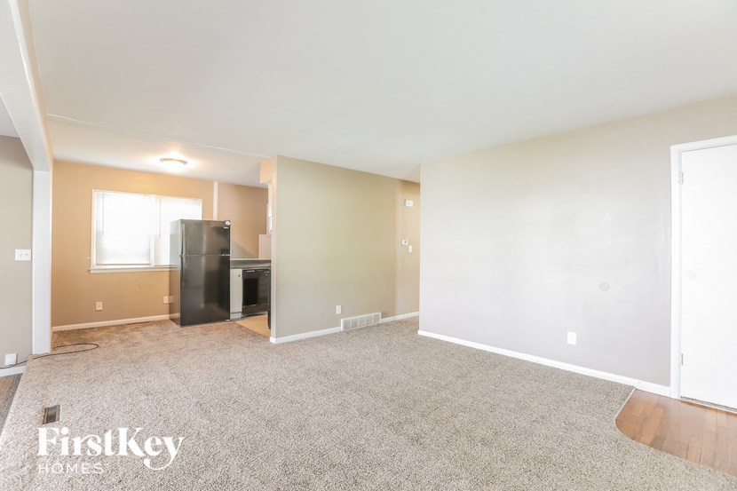 A spacious room with a carpeted floor and a refrigerator in the corner.