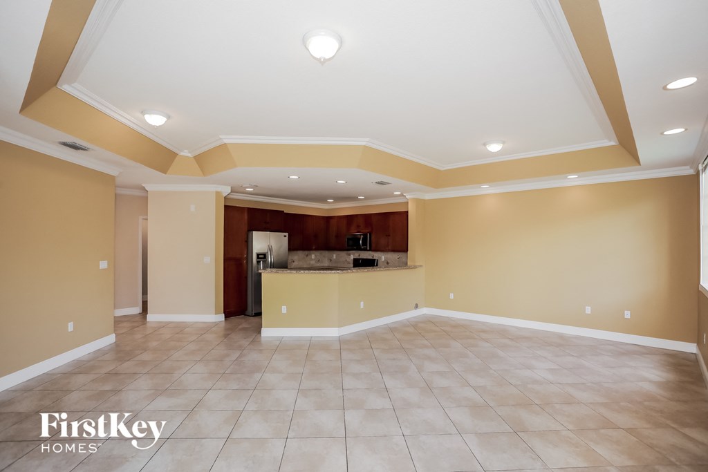 an empty living room with a kitchen in the corner