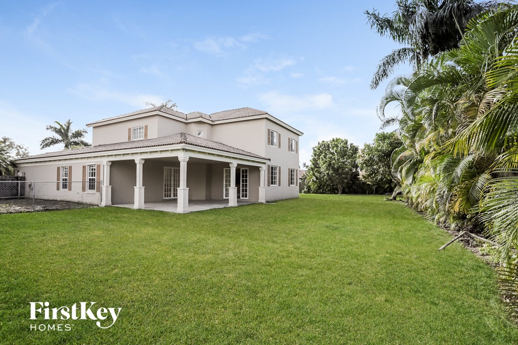 a large white house with a lawn and palm trees