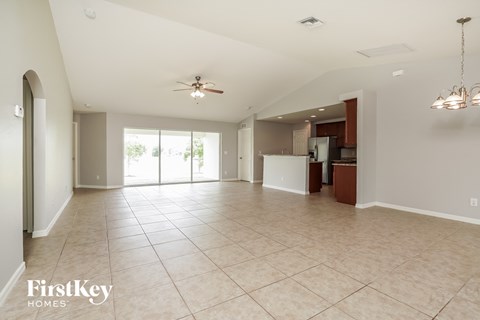 an empty living room with a kitchen and a ceiling fan
