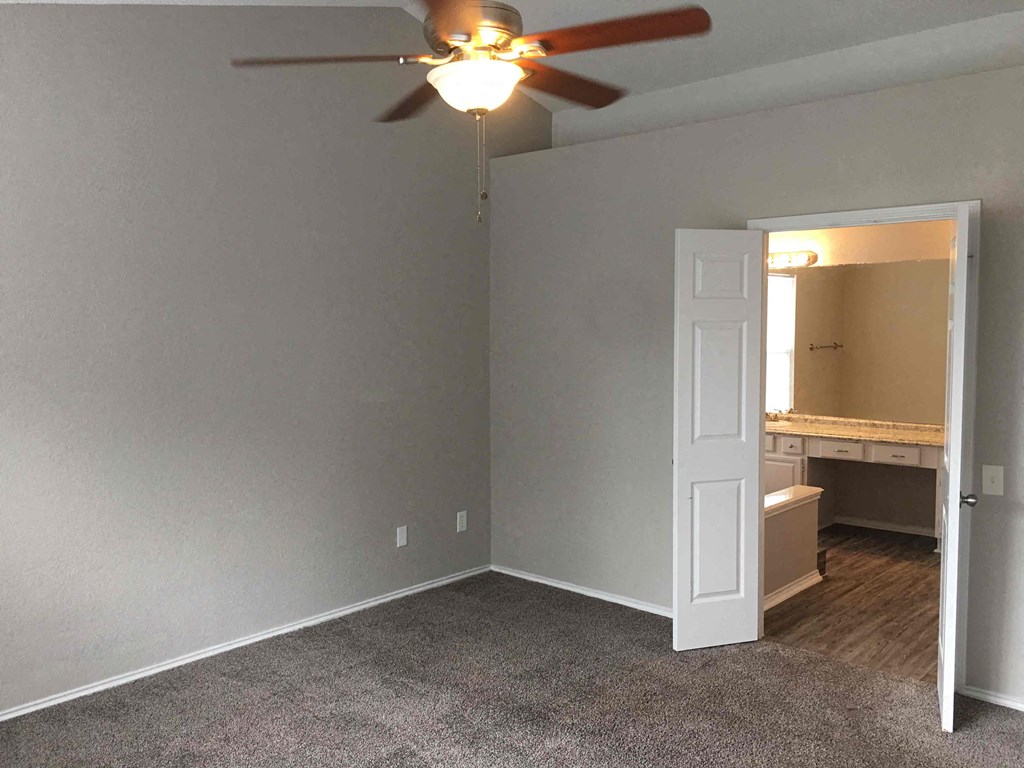 an empty room with a ceiling fan and a door to a bathroom