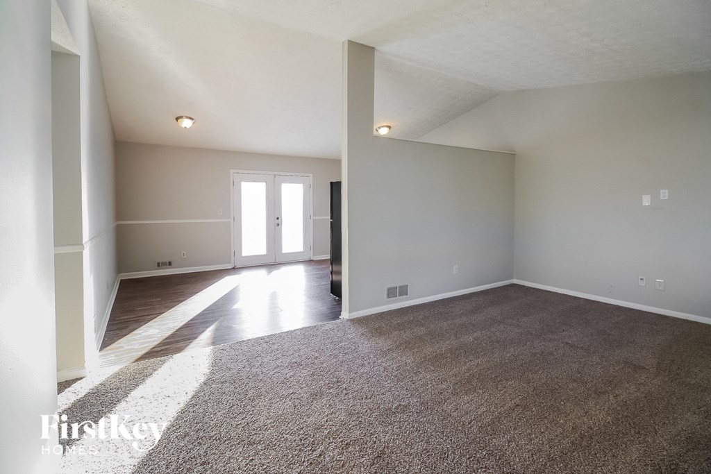 A large empty room with a carpeted floor and a door at the end.