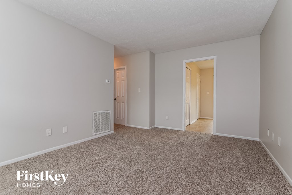 a spacious living room with carpeting and a door to a hallway