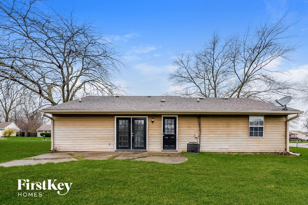 the front of a yellow house on a lawn with trees