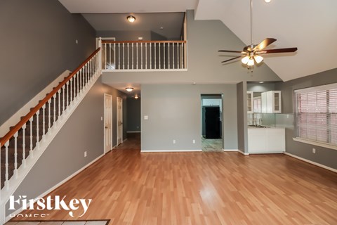 A spacious living room with a staircase and a ceiling fan.