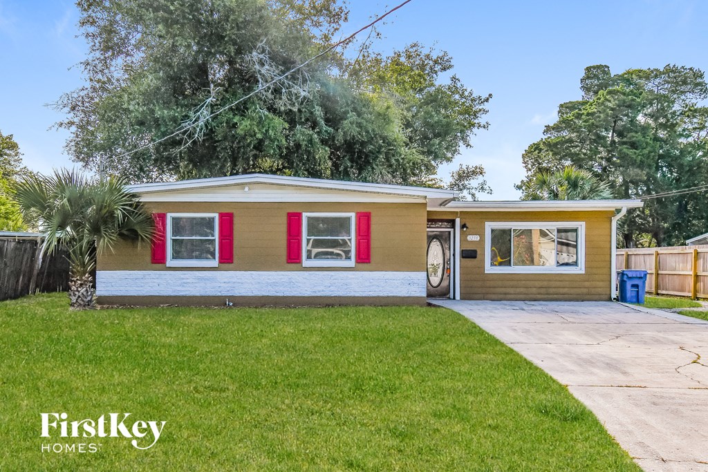 a small brown house with red shutters and a driveway