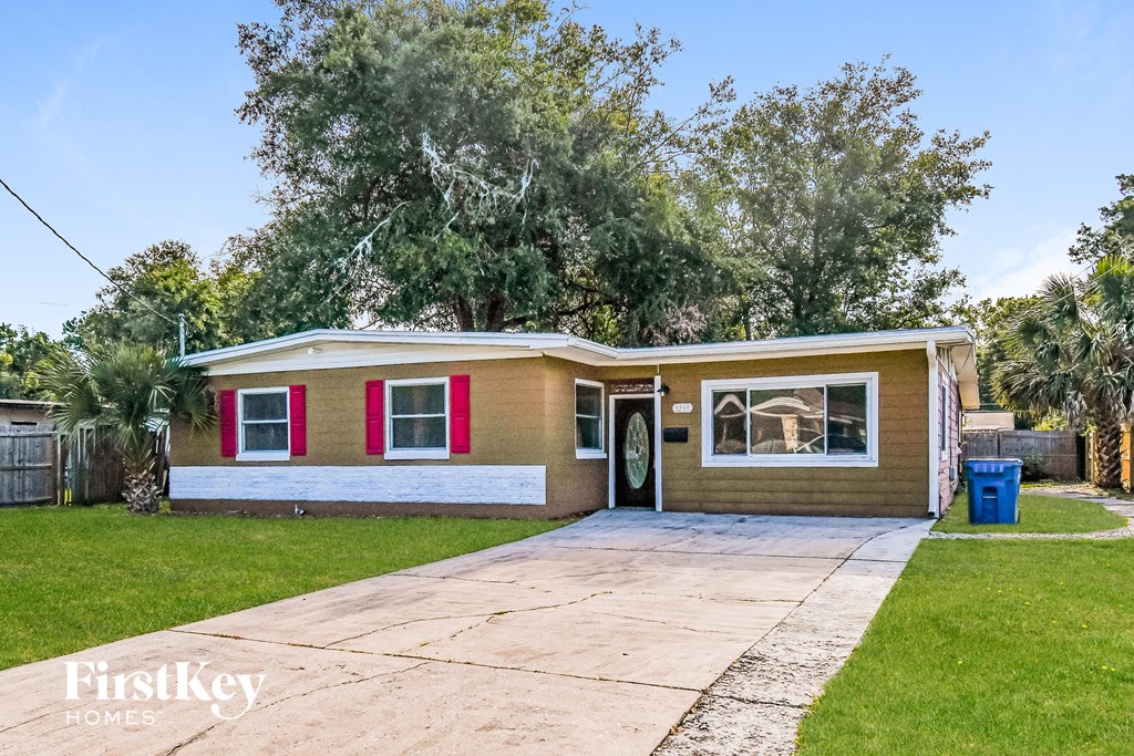 a small brown house with red shutters and a driveway
