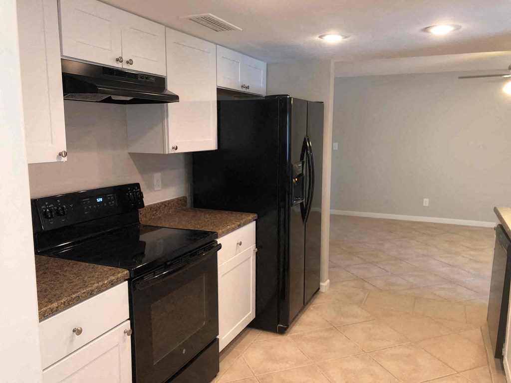 A black refrigerator stands in a kitchen with white cabinets and black appliances.