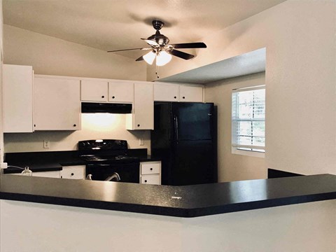 A black refrigerator sits in a kitchen with white cabinets.