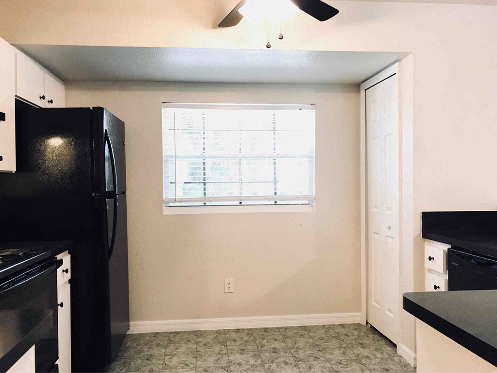 A kitchen with black appliances and a window with blinds.