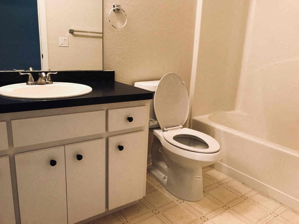 A white toilet is in a bathroom with a sink and a mirror.